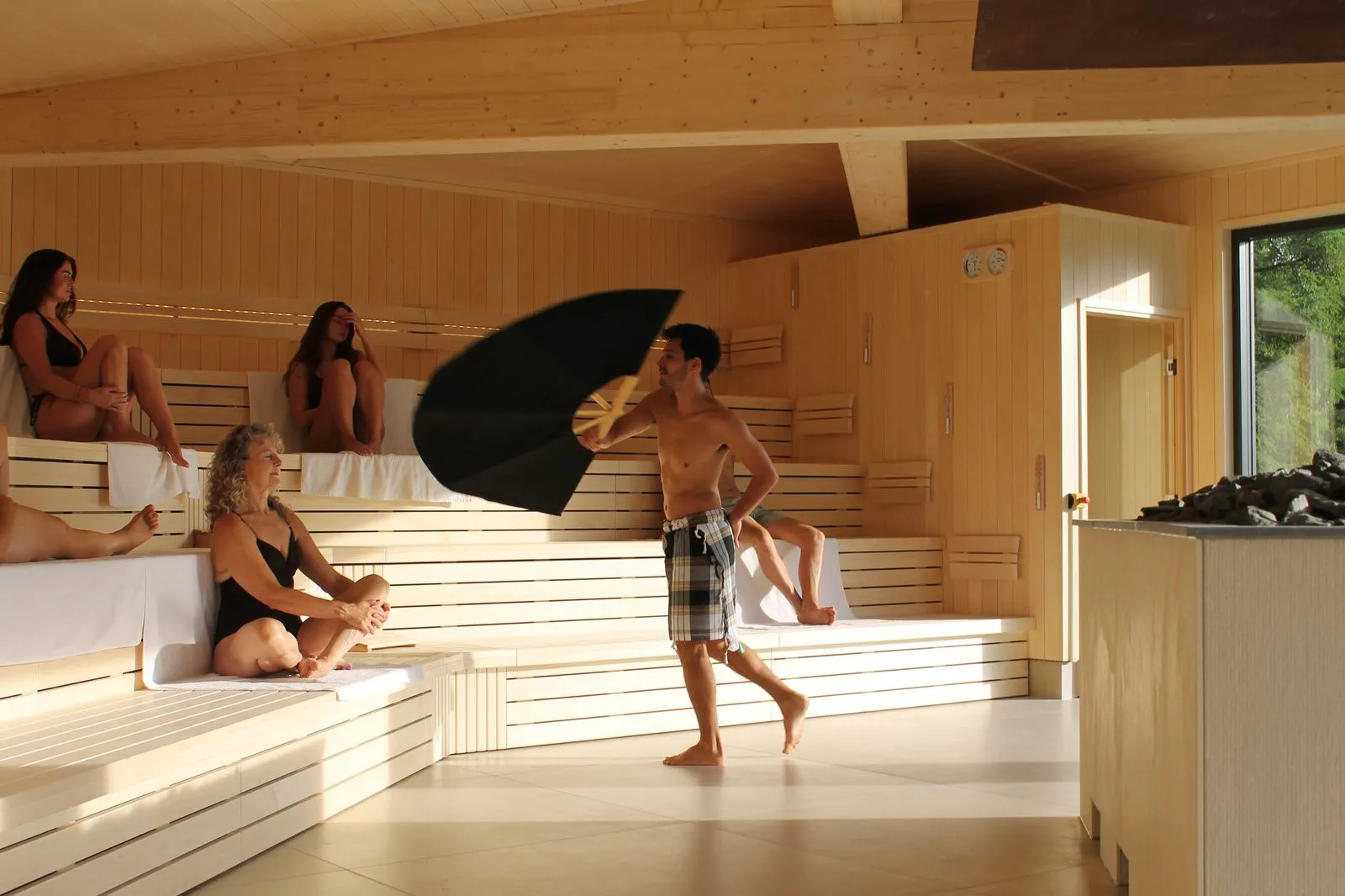 Saunameester zwaait met een handdoek tijdens een opgieting in Eir, de panorama-opgietsauna van Thermae 2000, met gasten op de tribunes en uitzicht door het grote raam
