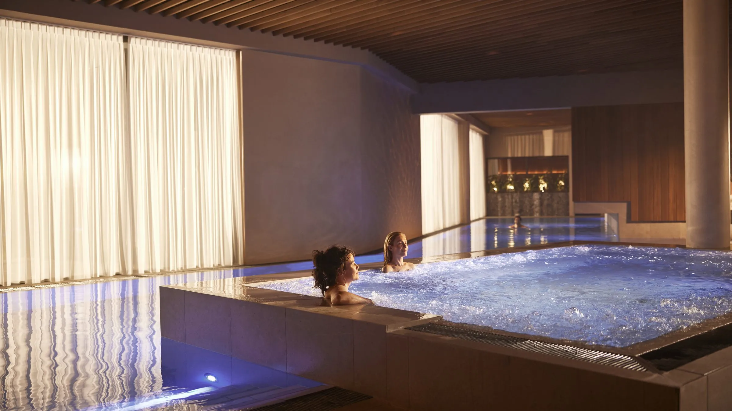 Het binnenbad van Thermen Maastricht met gordijnen en een verlichte waterrand