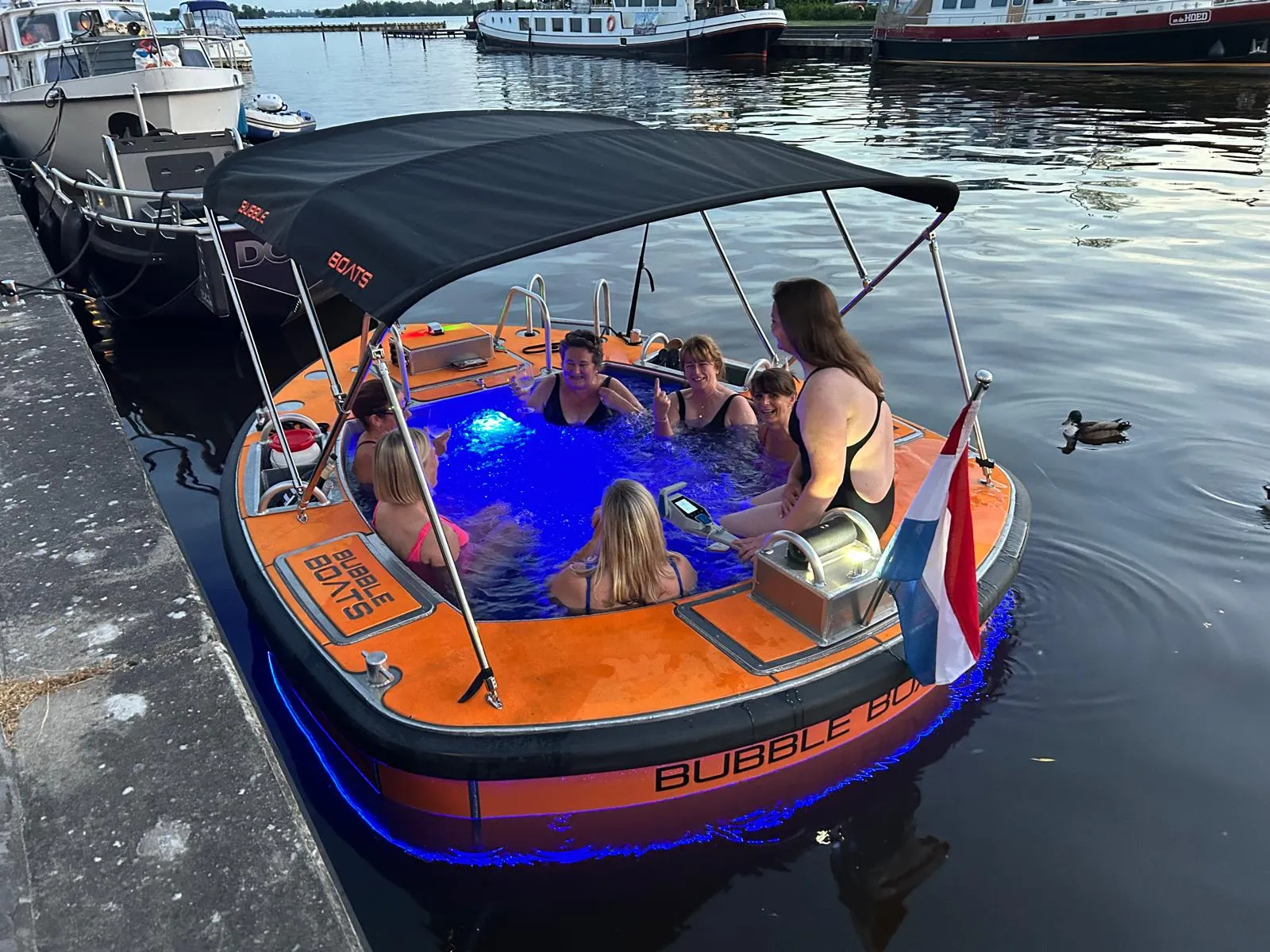 Een groep vrienden geniet 's avonds van een varende jacuzzi met blauw verlichte bubbels in Loosdrecht