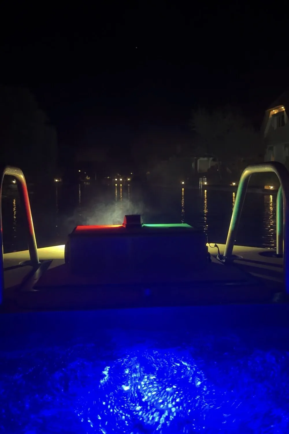 Uitzicht vanuit de varende jacuzzi over het donkere water van Loosdrecht, met blauw verlicht water op de voorgrond en lichtjes aan de oever